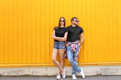 Photo of Young couple wearing black t-shirts near color wall on street