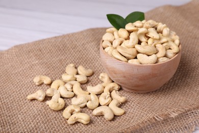 Photo of Tasty cashew nuts and green leaves on table, closeup. Space for text