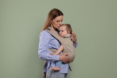 Photo of Mother holding her child in sling (baby carrier) on olive background