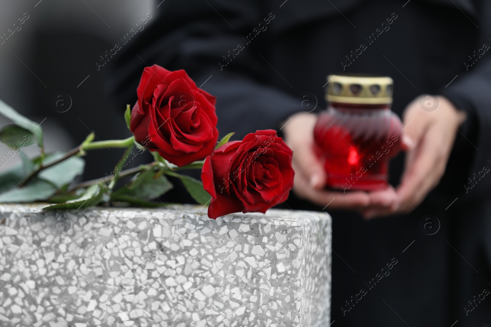 Photo of Woman with candle outdoors, focus on red roses. Funeral ceremony