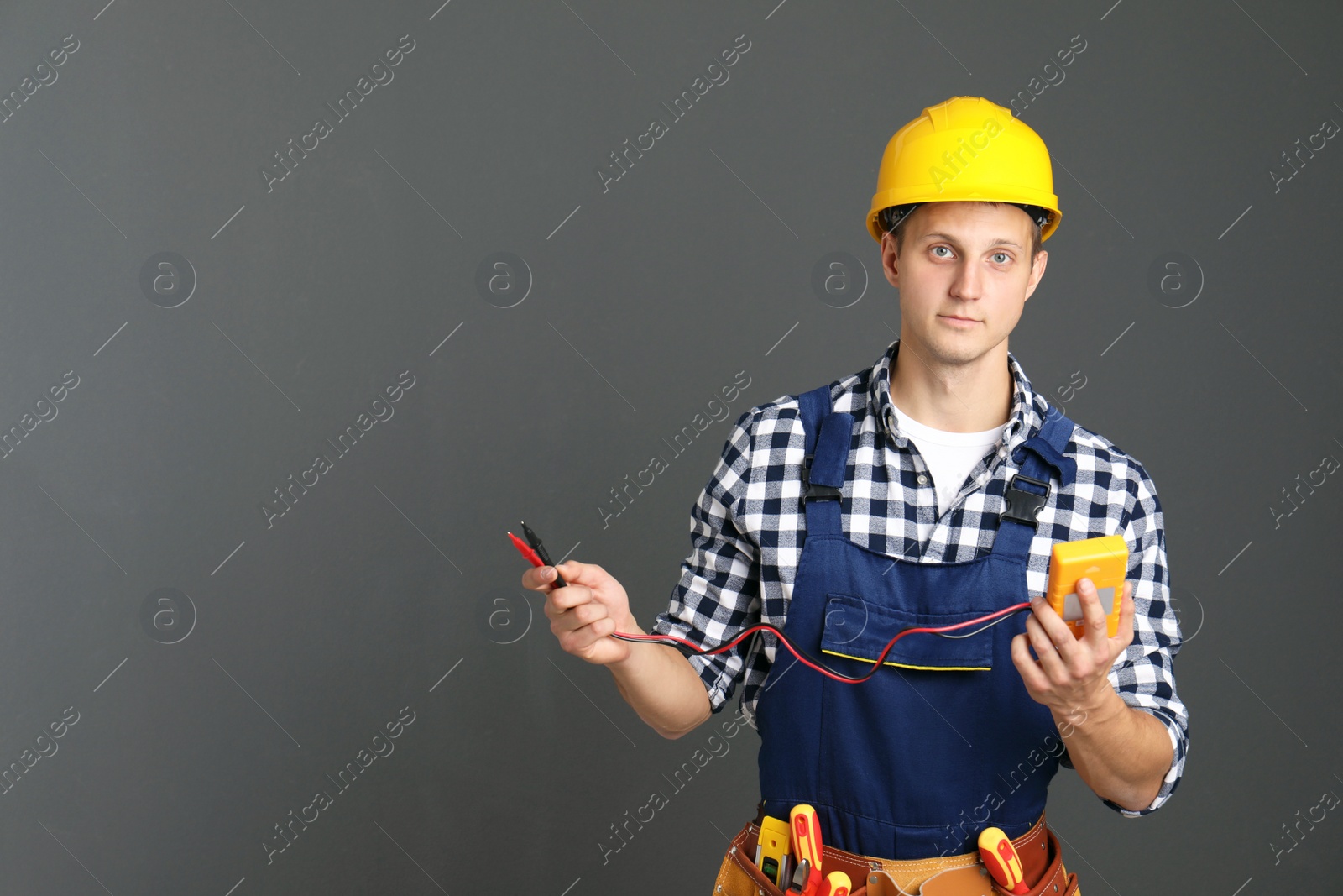 Photo of Electrician with multimeter wearing uniform on gray background. Space for text