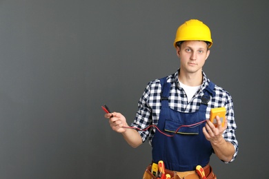 Photo of Electrician with multimeter wearing uniform on gray background. Space for text