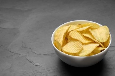 Photo of Bowl of potato chips on grey table. Space for text