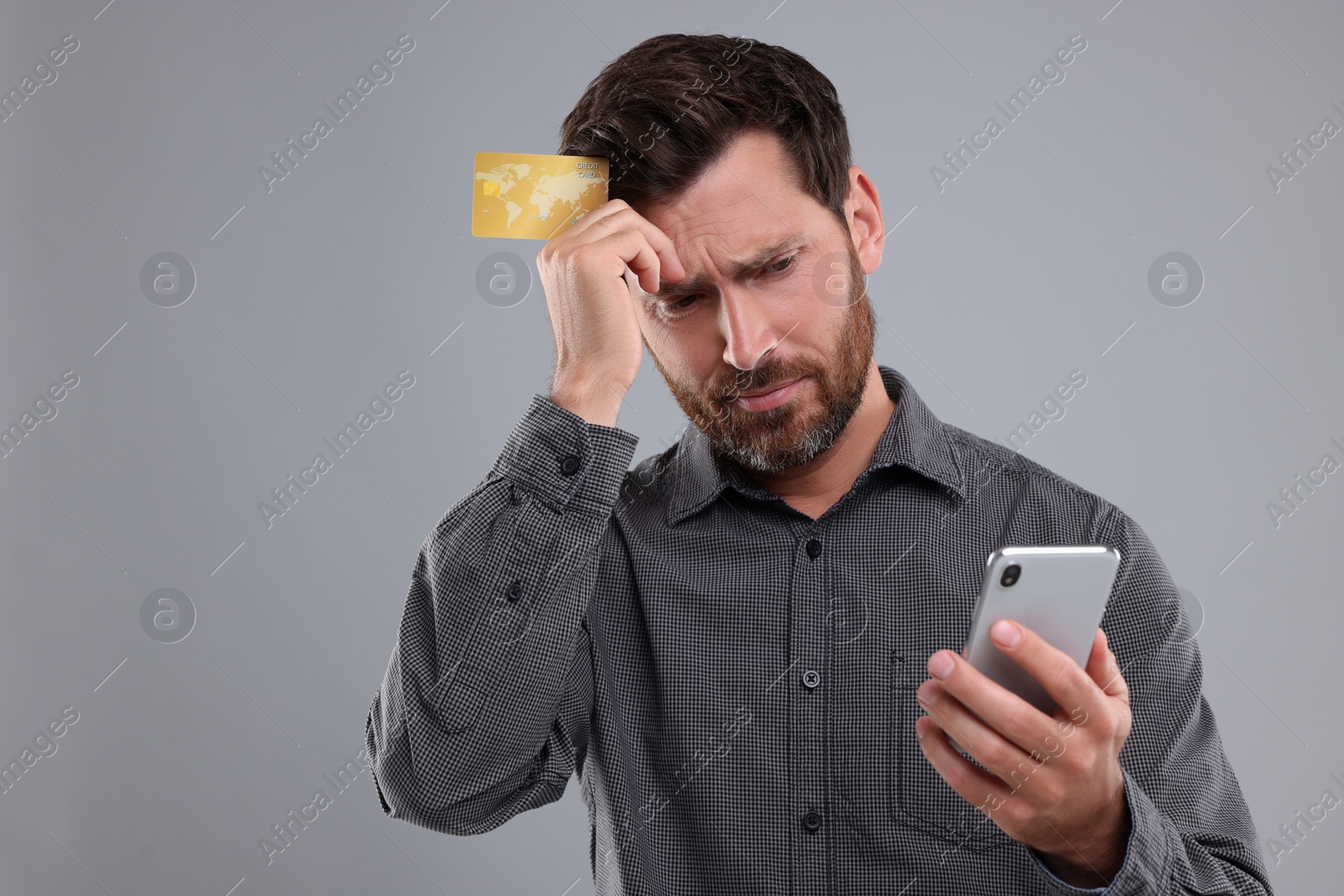 Photo of Upset man with smartphone and credit card on light grey background. Be careful - fraud