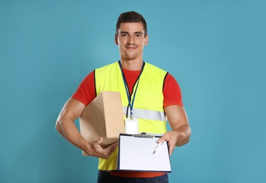 Photo of Happy young courier with parcel and clipboard on blue background