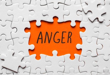 Photo of White puzzle pieces and word ANGER written on orange background, flat lay