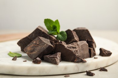 Tasty dark chocolate pieces with mint on white board, closeup