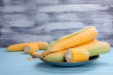 Photo of Plate with tasty sweet corn cobs on wooden table