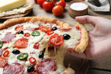 Man taking slice of delicious pizza Diablo at wooden table, closeup