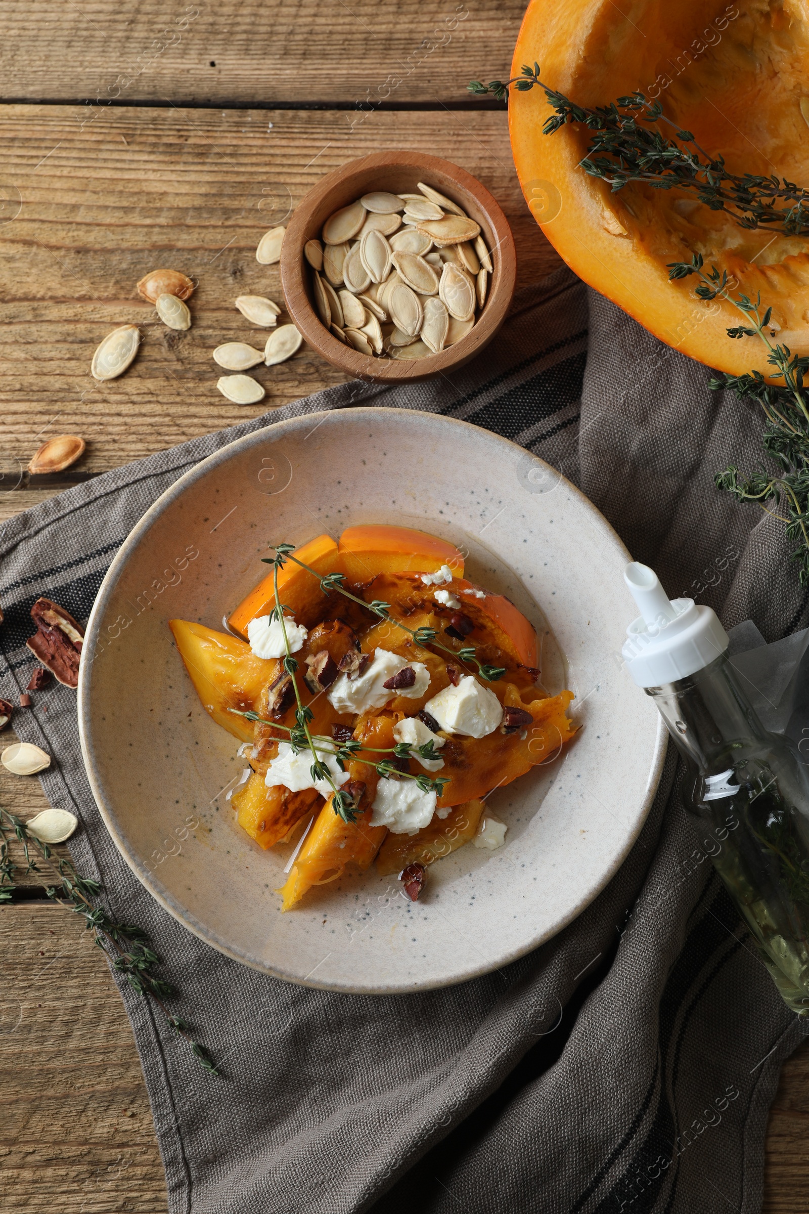 Photo of Baked pumpkin slices served with cheese, thyme and pecans on wooden table, flat lay