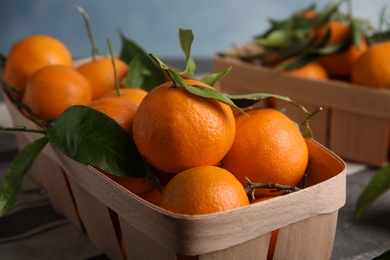 Photo of Fresh ripe tangerines with green leaves in crate on table