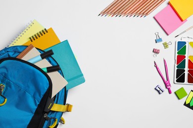 Photo of Backpack with different school stationery on white background, flat lay. Space for text