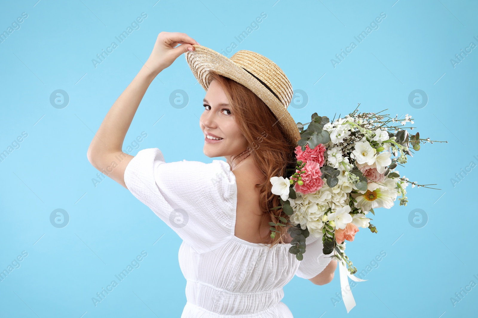 Photo of Beautiful woman in straw hat with bouquet of flowers on light blue background