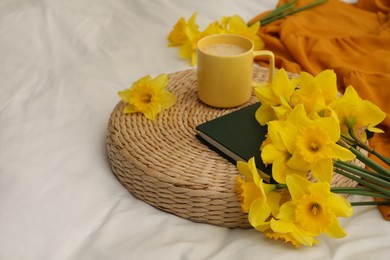 Bouquet of beautiful daffodils, book and coffee on bed, space for text