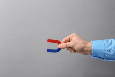 Man holding magnet on grey background, closeup. Space for text