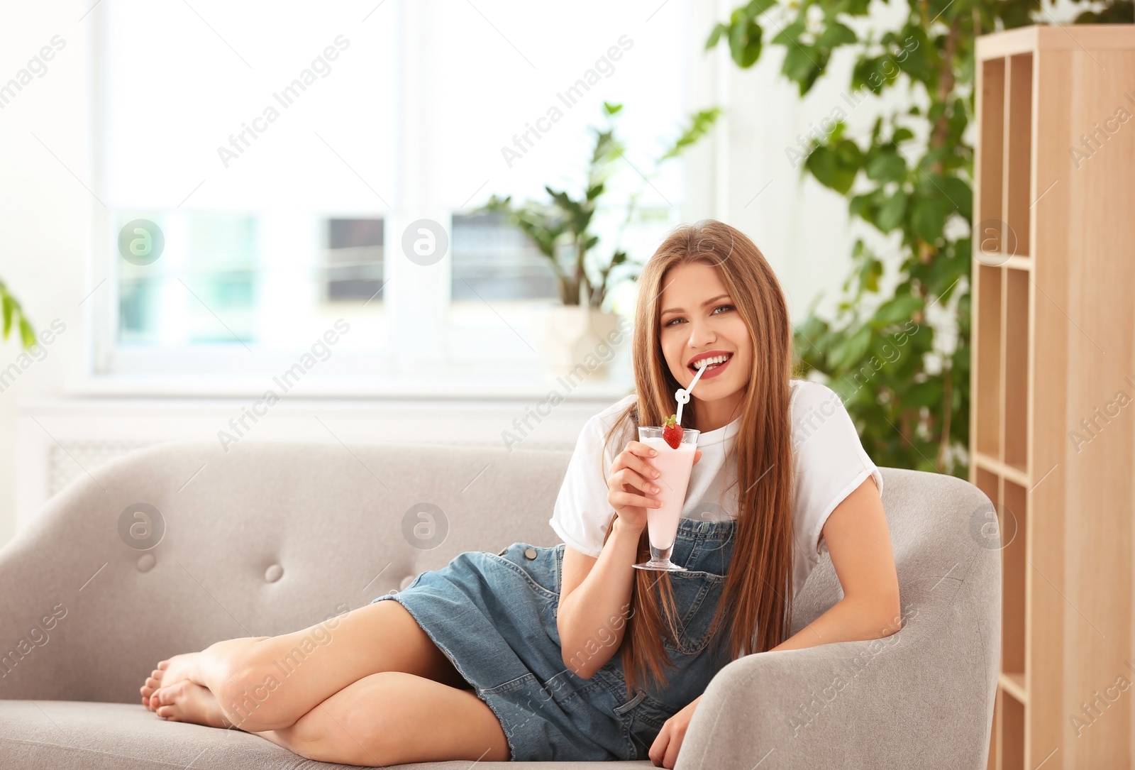 Photo of Young woman with glass of delicious milk shake indoors