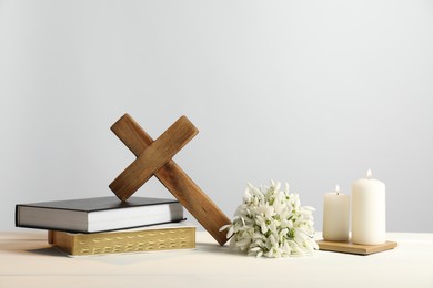 Photo of Burning church candles, wooden cross, ecclesiastical books and flowers on white table