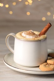 Photo of Cup of delicious eggnog with cinnamon and cookies on wooden table