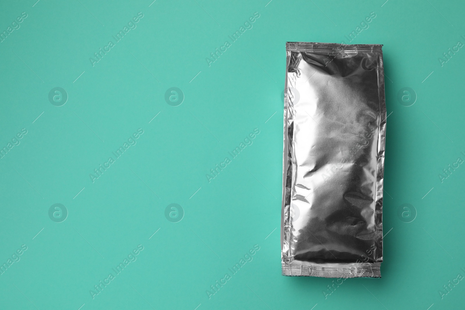 Photo of Blank foil package on turquoise background, top view. Space for text