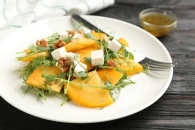 Delicious persimmon salad with feta cheese and walnuts on wooden table, closeup