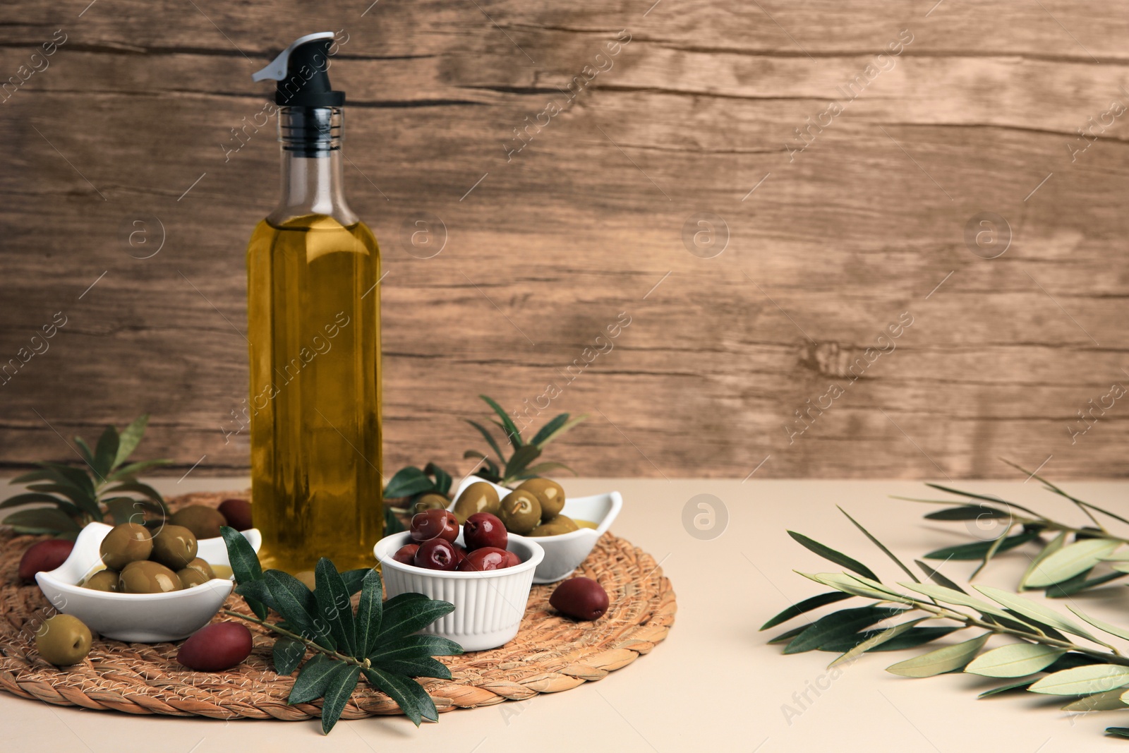 Photo of Bottle of oil, olives and tree twigs on beige table, space for text