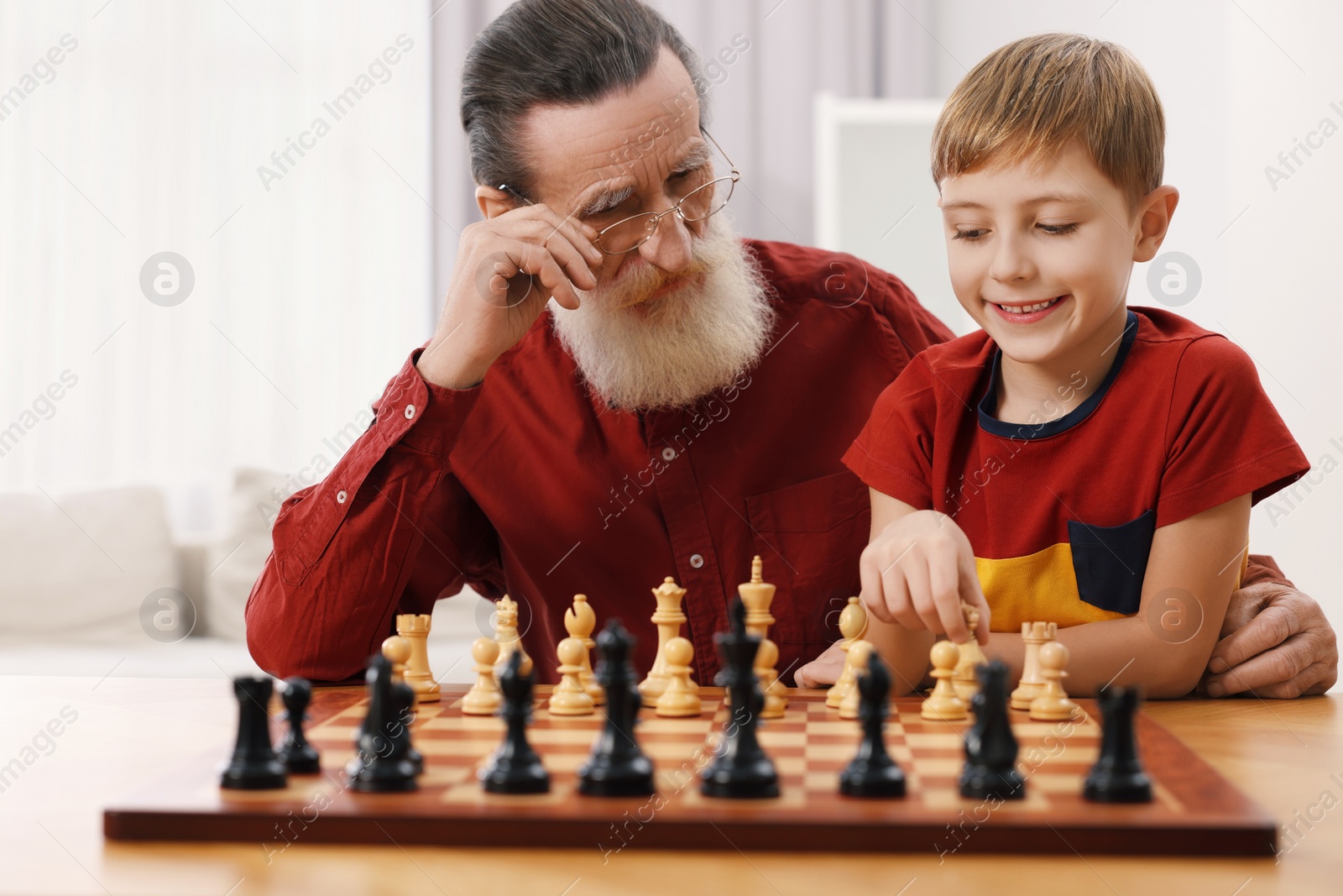 Photo of Senior man teaching his grandson to play chess at home