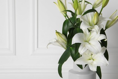 Beautiful bouquet of lily flowers in vase near white wall, space for text