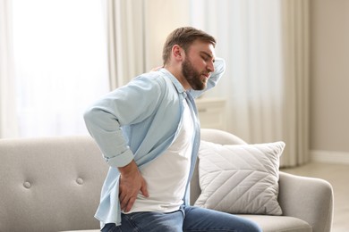 Photo of Man suffering from back pain at home. Bad posture problem