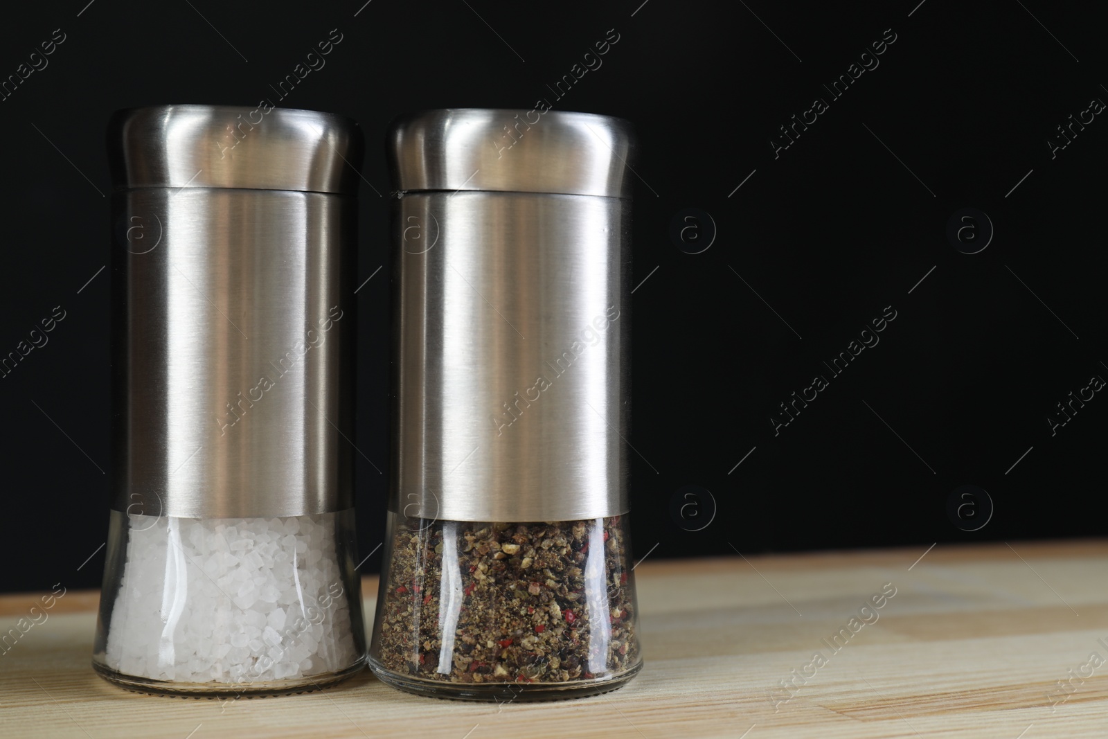 Photo of Salt and pepper shakers on light wooden table against black background, closeup. Space for text