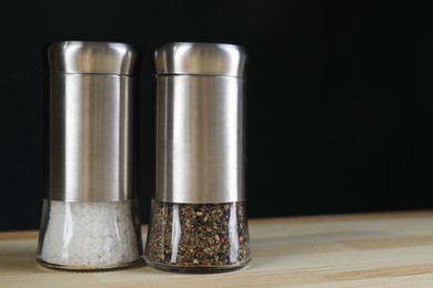 Salt and pepper shakers on light wooden table against black background, closeup. Space for text