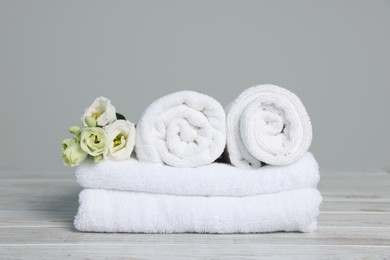 Photo of Soft white towels with flowers on wooden table against grey background