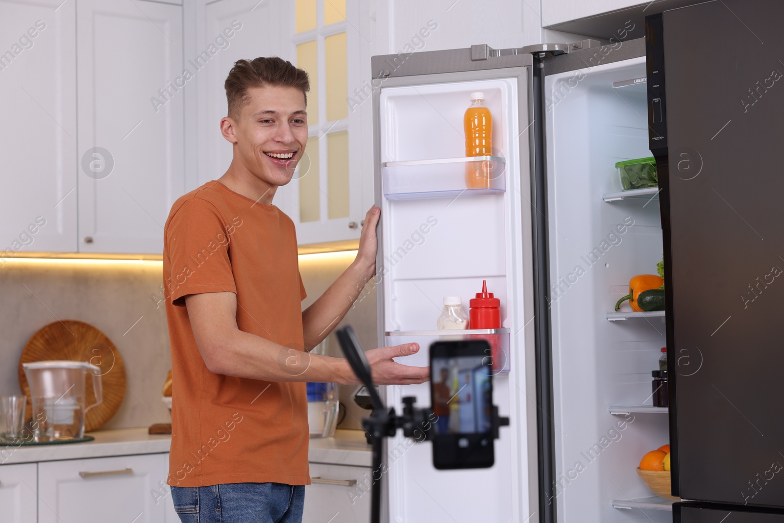 Photo of Smiling food blogger explaining something while recording video in kitchen