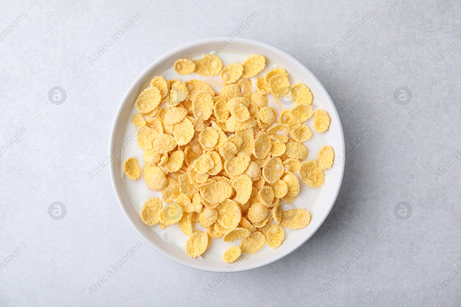 Photo of Breakfast cereal. Corn flakes and milk in bowl on light grey table, top view