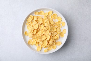 Photo of Breakfast cereal. Corn flakes and milk in bowl on light grey table, top view