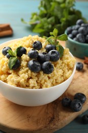 Tasty millet porridge with blueberries and mint in bowl on wooden table, closeup