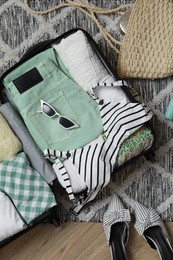 Photo of Open suitcase with summer clothes, accessories and shoes on floor, flat lay