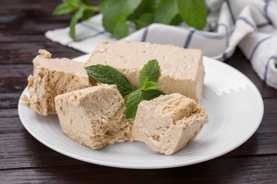 Photo of Plate with pieces of tasty halva and mint on wooden table, closeup