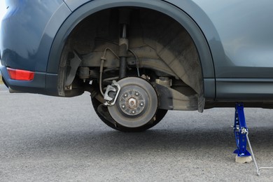 Photo of Car lifted by scissor jack without wheel outdoors, closeup. Tire puncture