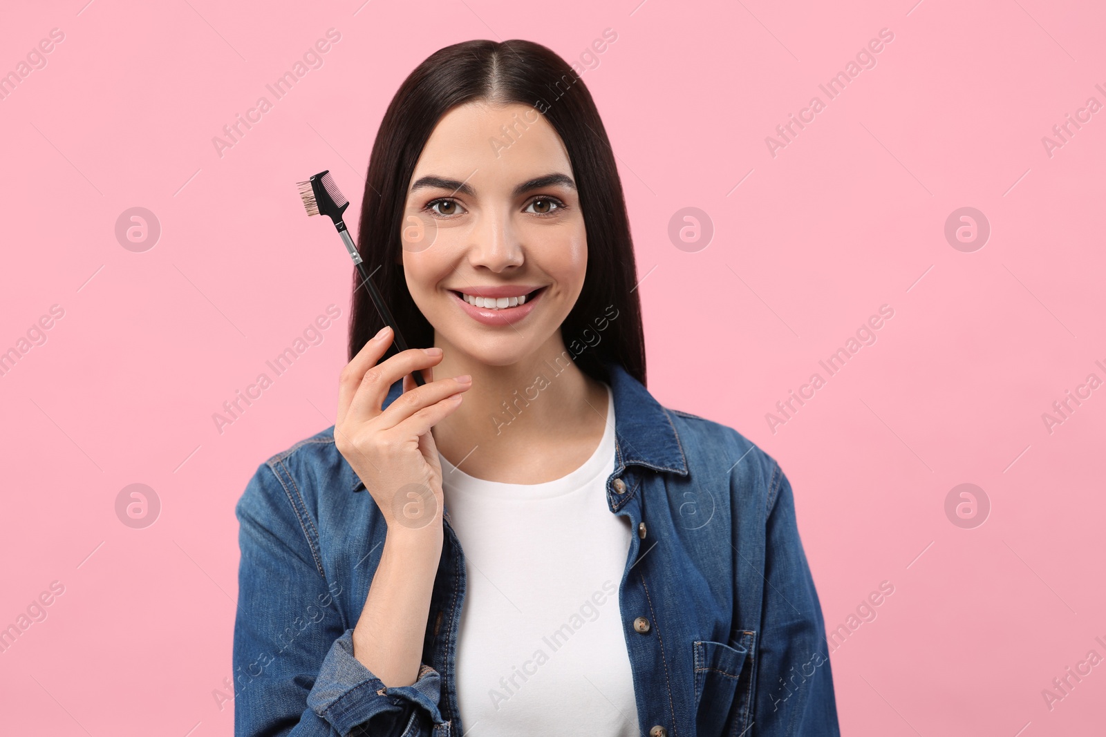 Photo of Happy woman with makeup eyebrow brush on pink background