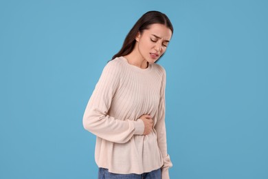 Photo of Woman suffering from abdominal pain on light blue background. Unhealthy stomach