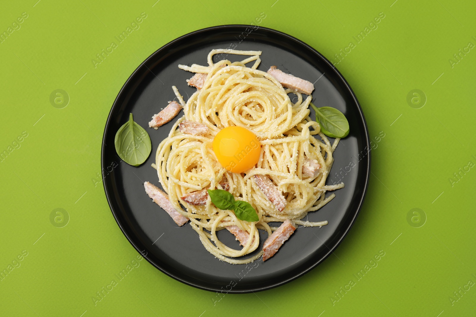 Photo of Plate of tasty pasta Carbonara with basil leaves on light green background, top view