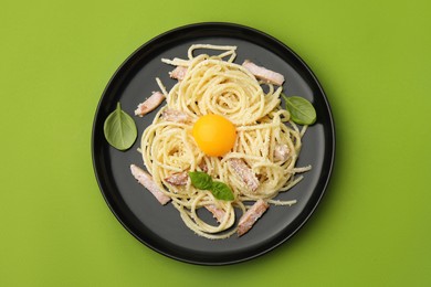 Plate of tasty pasta Carbonara with basil leaves on light green background, top view