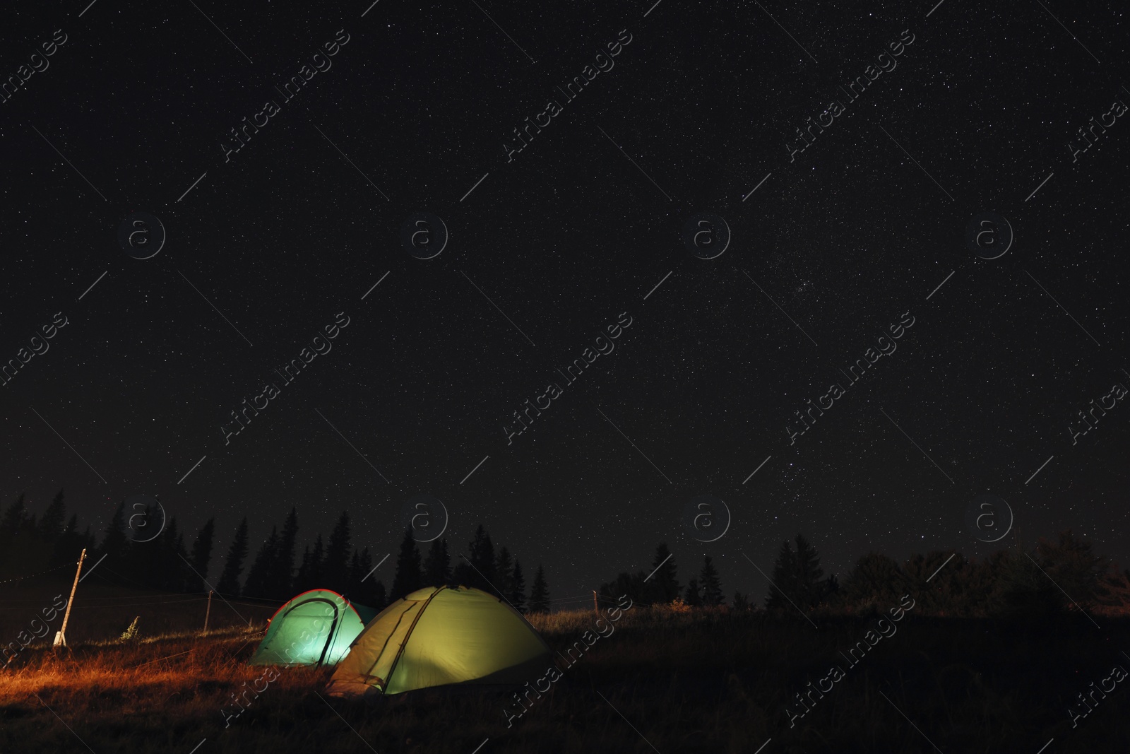 Photo of Two color camping tents near forest under sky full of stars at night