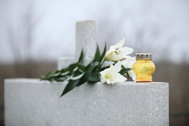 Photo of White lilies and candle on light grey granite tombstone outdoors. Funeral ceremony