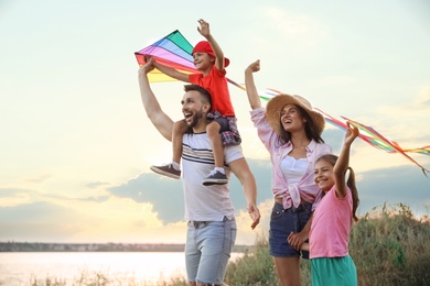 Photo of Happy parents and their children playing with kites outdoors at sunset. Spending time in nature