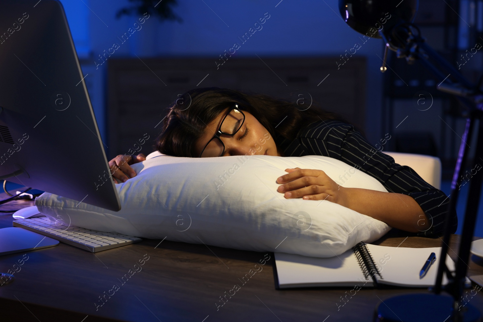 Photo of Tired overworked businesswoman napping with pillow at night in office