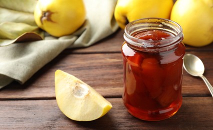 Tasty homemade quince jam in jar and fruits on wooden table, closeup