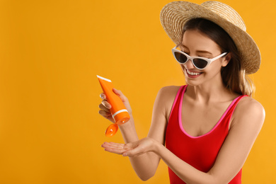 Young woman applying sun protection cream on orange background