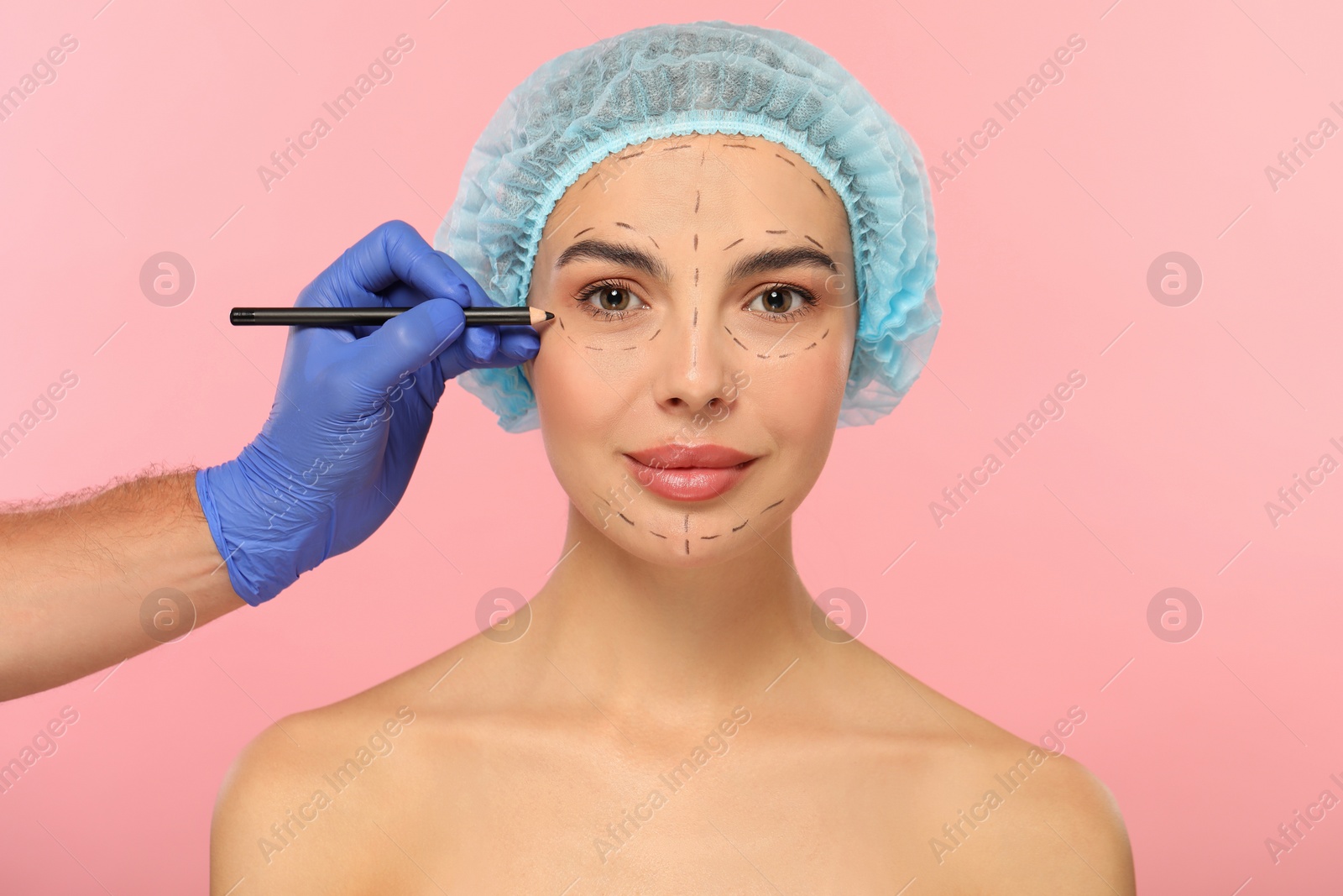 Photo of Doctor with pencil preparing patient for cosmetic surgery operation on pink background