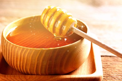 Image of Natural honey in wooden bowl and dipper on table under sunlight, closeup